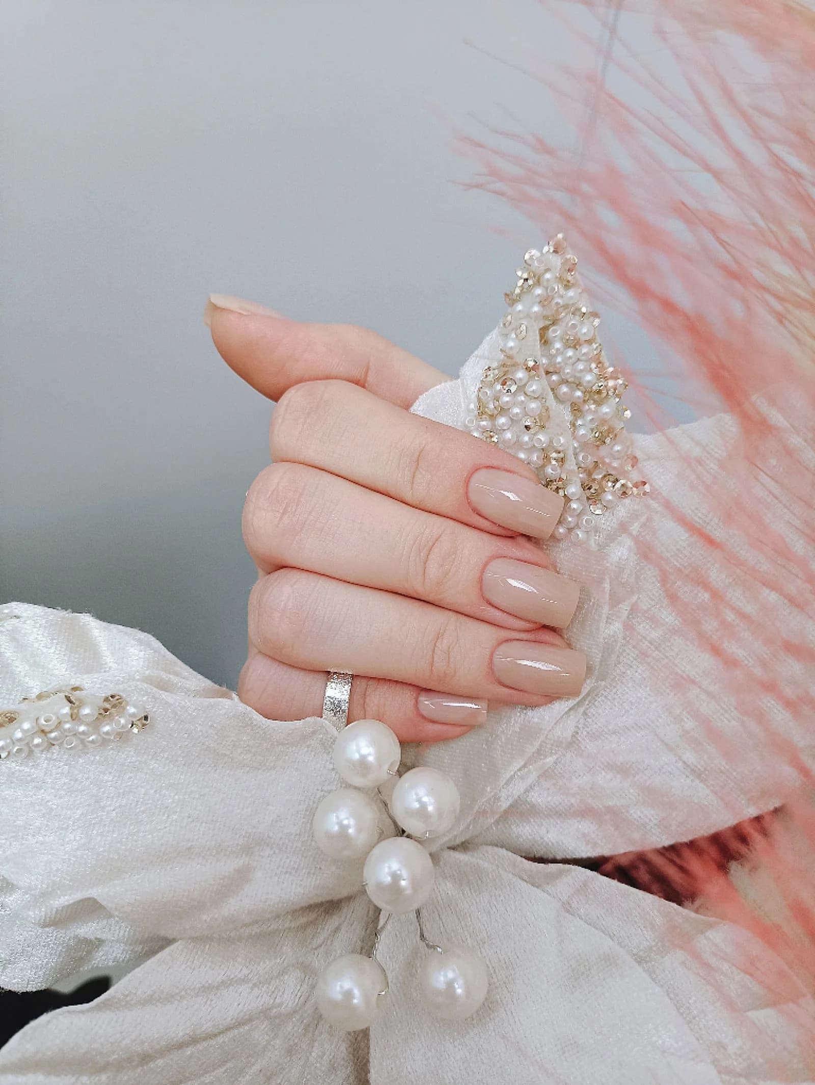 Glossy nude manicure with pearls and soft blush fabric